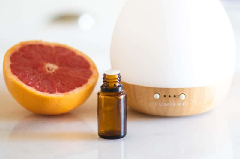 amber essential oil bottle in front of a grapefruit and a white diffuser 