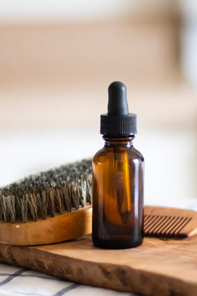 homemade beard oil in convenient dropper bottle with wooden beard comb and smooth bristle brush 