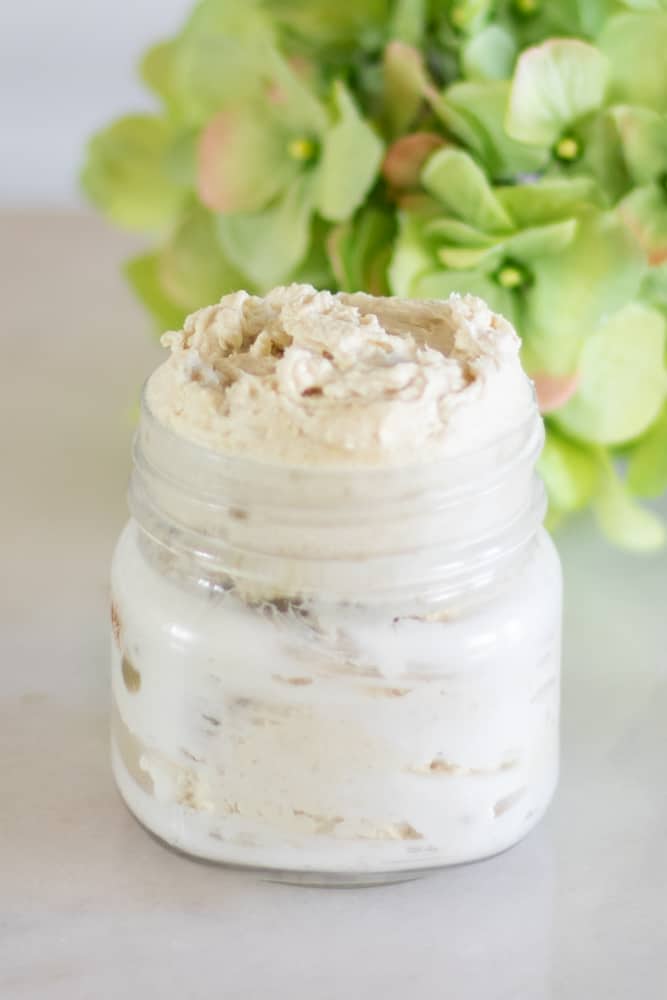 homemade glowing skin body butter in glass jar with lavender petals in background
