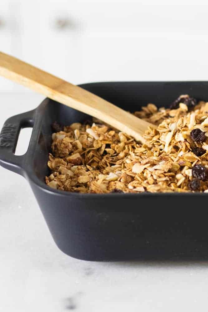 homemade granola in black baking dish with wooden spoon in it 