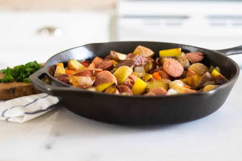 sausage, potatoes and onions chopped up in a cast-iron skillet on marble table top