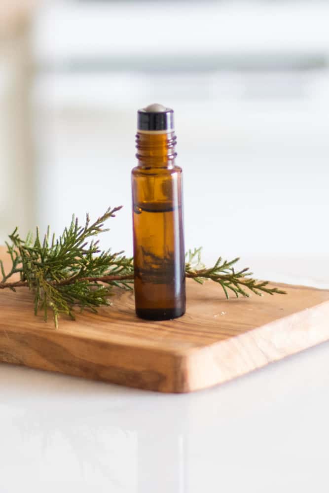 essential oil roller bottle on wood board with pine needles around it 