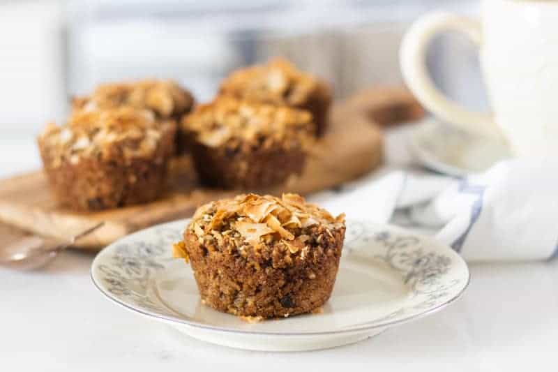 applesauce muffins topped with shredded coconut oil on small glass plate with more muffins on wooden cutting board in background