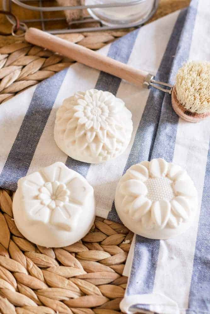 Handmade white soap bars in shape of flowers on blue and white tea towel. 