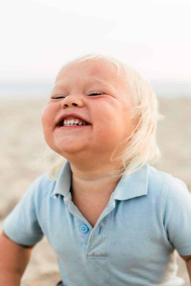 Toddler boy in blue polo smiling on the beach. 