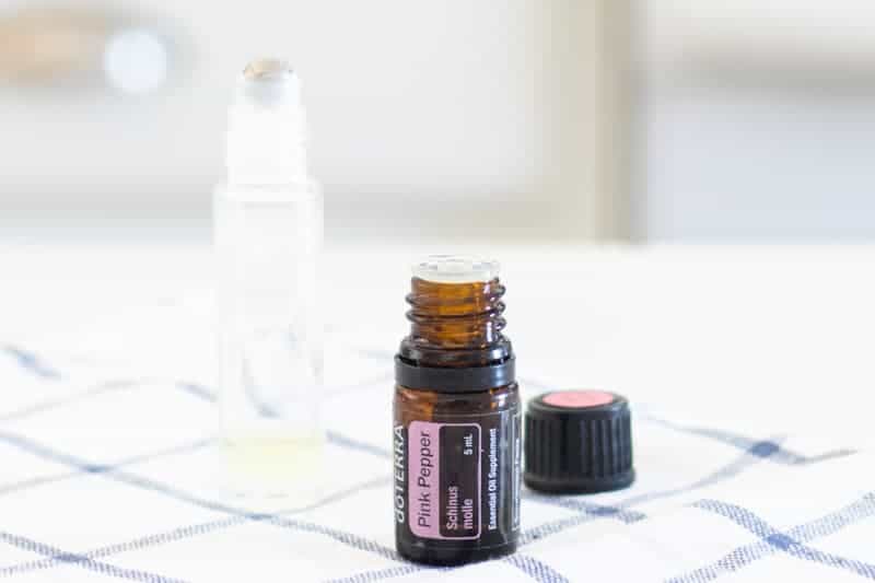 Bottle of pink pepper essential oil sitting on white and blue tea towel.