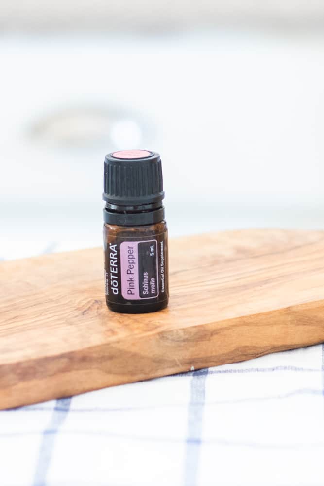 DoTERRA pink pepper essential oil bottle on wooden cutting board. 