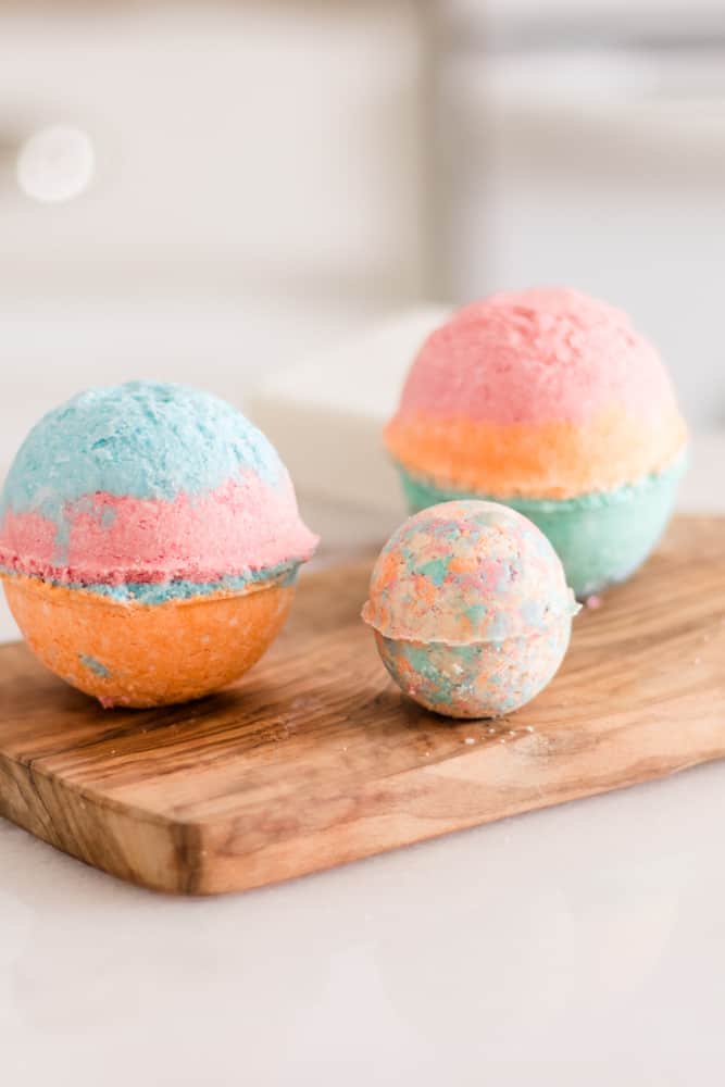 Three bright colored bath bombs on wooden cutting board. 