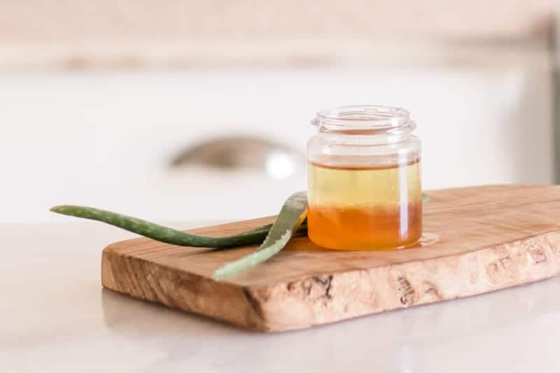 Aloe leaves and aloe hair mask sitting on wood board on white table.