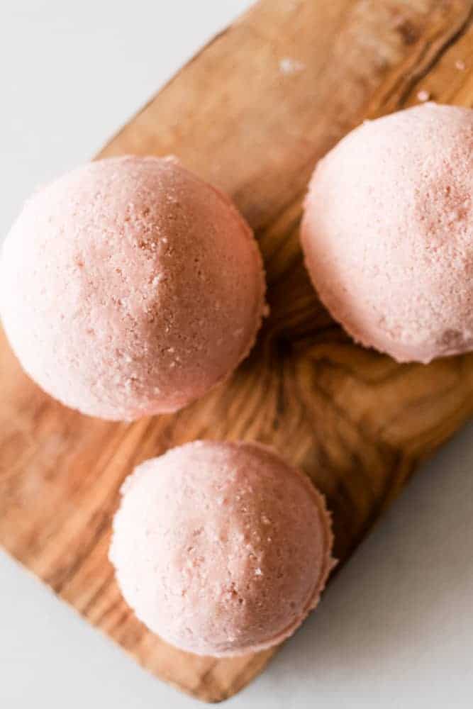 Three pink homemade bath bombs on a wood cutting board. 