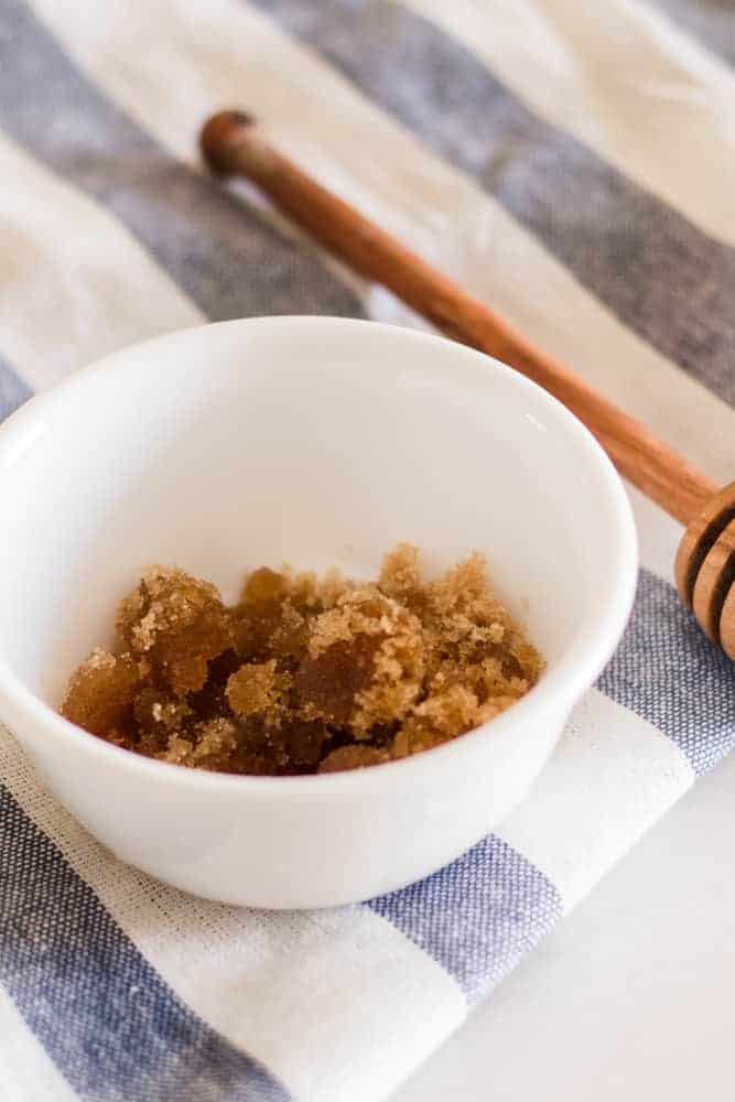 Brown sugar scalp scrub in white bowl with wooden honey dipper.