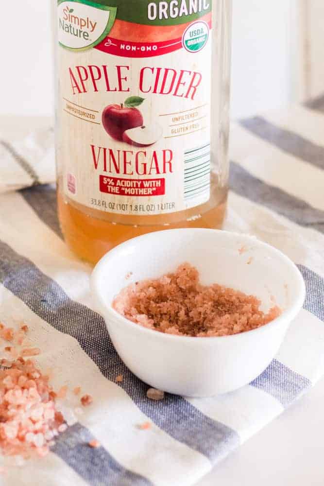 Pink salt scrub for dry scalp in a white bowl with apple cider vinegar.