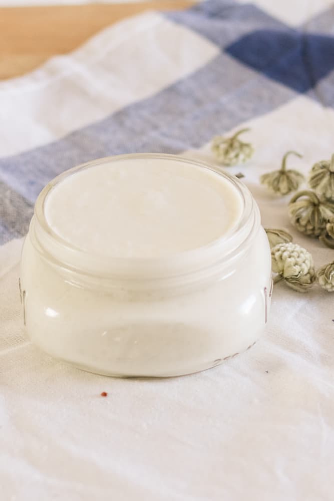 Wide mouth mason jar of goat milk lotion on tea towel.