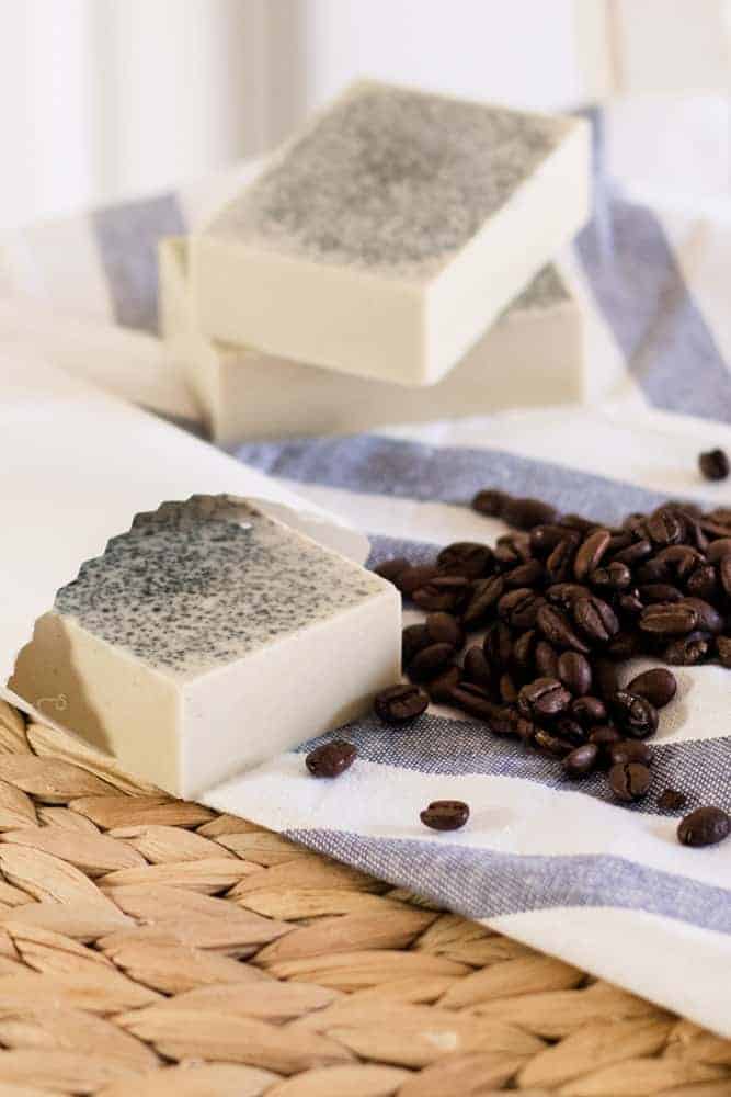 Goat milk coffee melt and pour soap bar in white paper and whole coffee beans around it. 