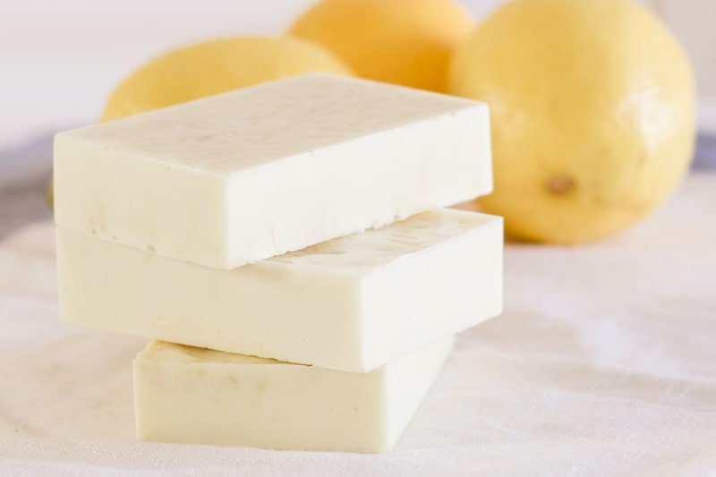 Lemon soap bars stacked on white tea towel with fresh lemons behind them. 