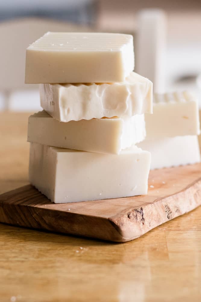 Four shampoo bars stacked on top of wooden cutting board. 