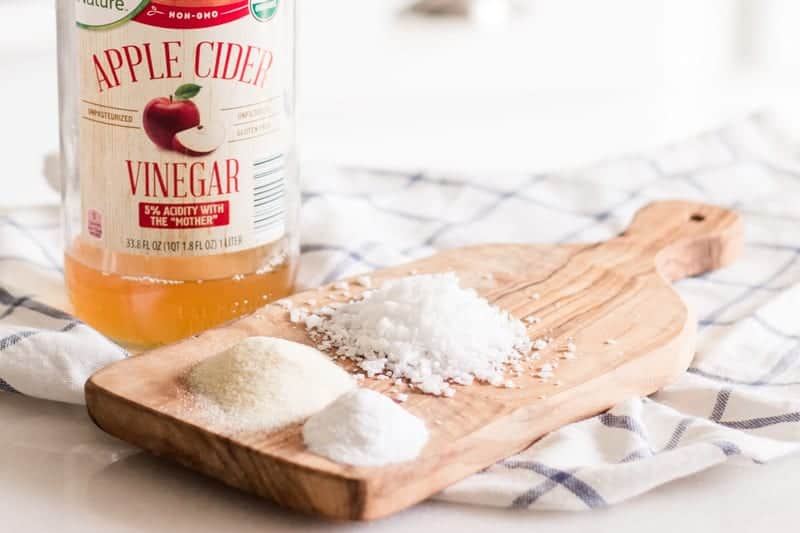 Apple cider vinegar and wax emulsifiers sitting on white marble table with blue and white tea towel. 