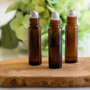 Three amber roller bottles on a wooden board with green flowers behind them.