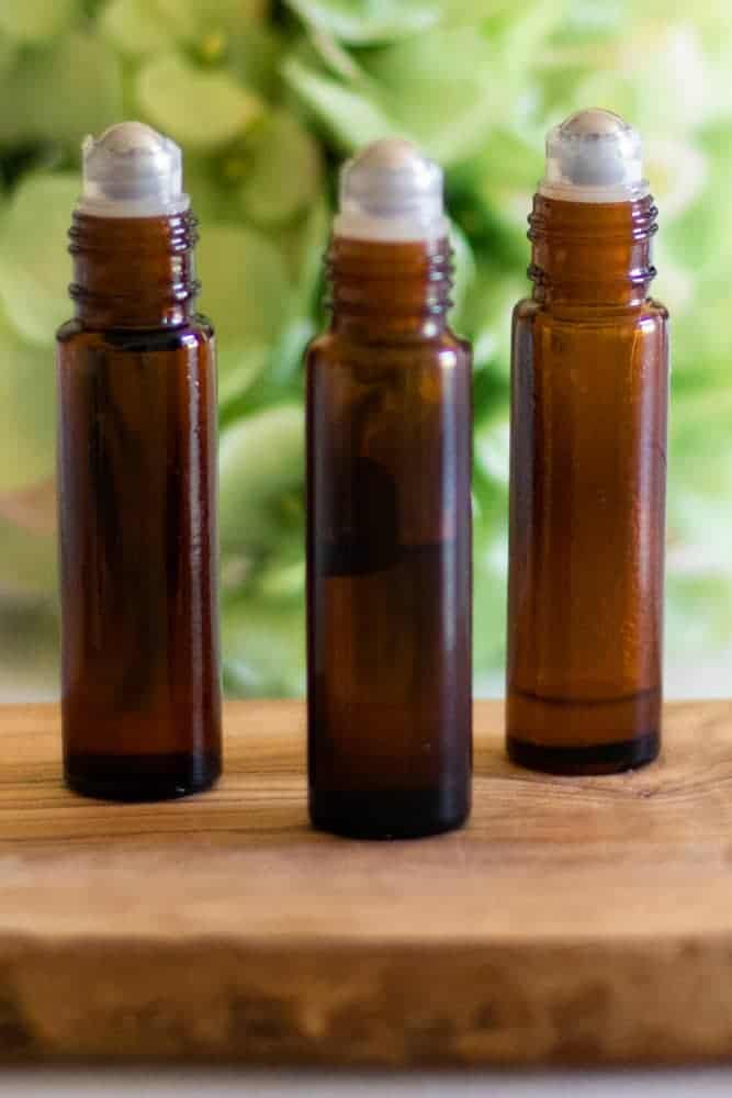 Three essential oil roller bottles standing on wooden board with green  plant behind it. 