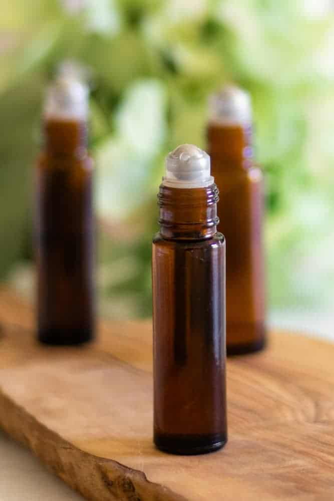 three essential oil roller bottles standing on wooden cutting board.