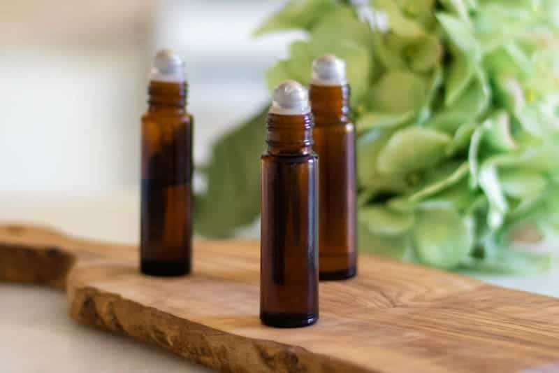 Essential oil roller bottles in front of green flowers.