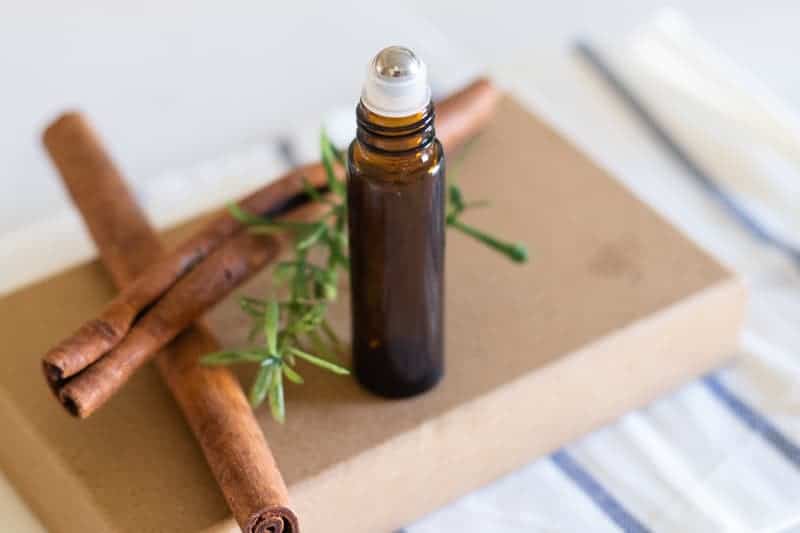 Amber roller bottle standing on box with cinnamon sticks and rosemary behind it. 