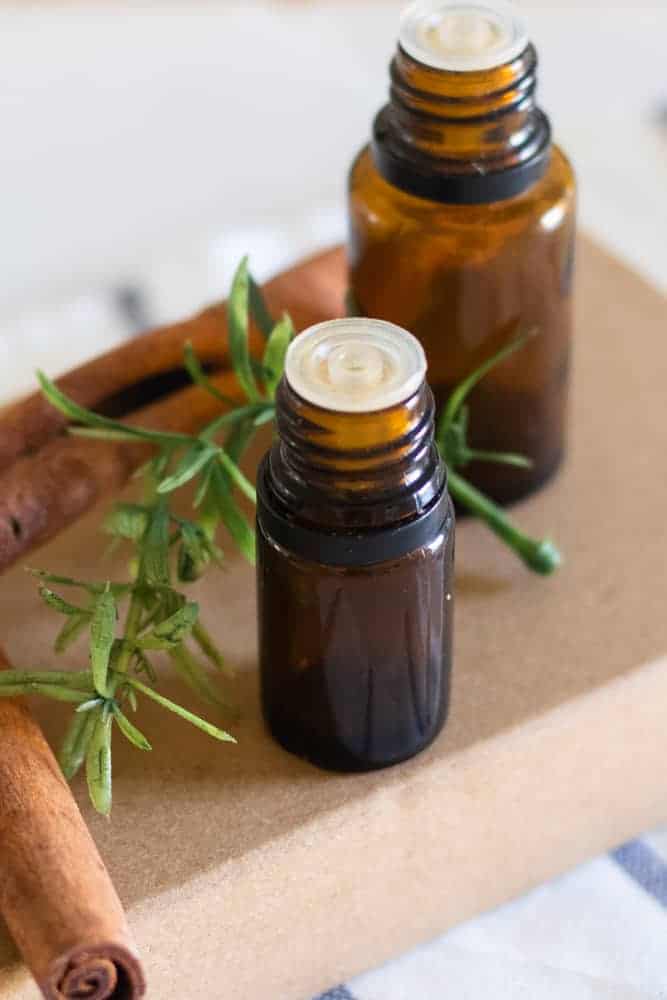 Essential oil bottles on cardboard box with rosemary sprig behind them.
