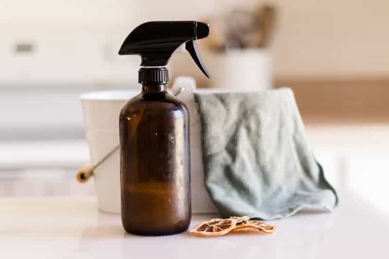 DIY dusting spray in glass spray bottle sitting on kitchen table.