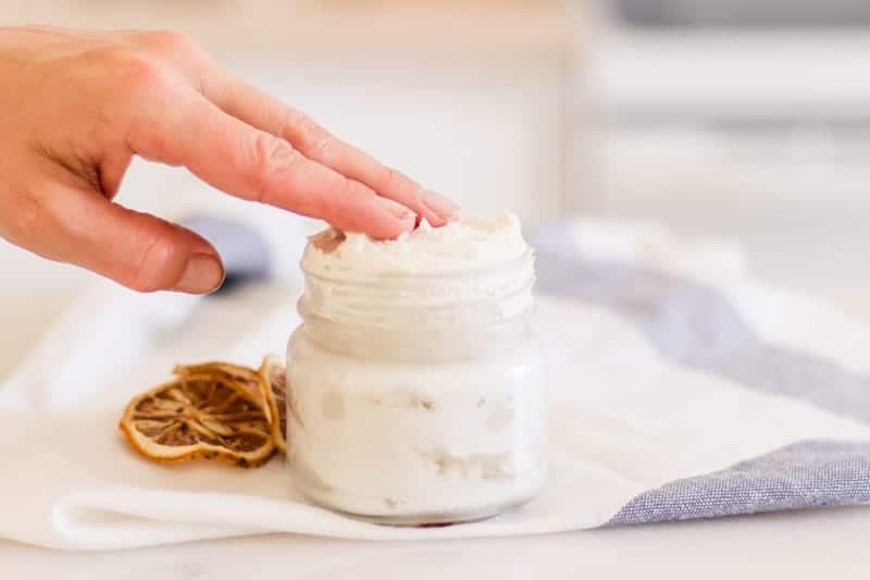 Women's hand in jar of homemade hand cream. 