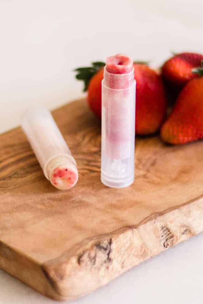 Homemade strawberry chapstick in clear tubes on wooden board. 