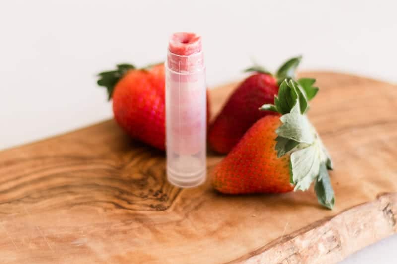 Clear tube of strawberry chapstick with fresh strawberries.