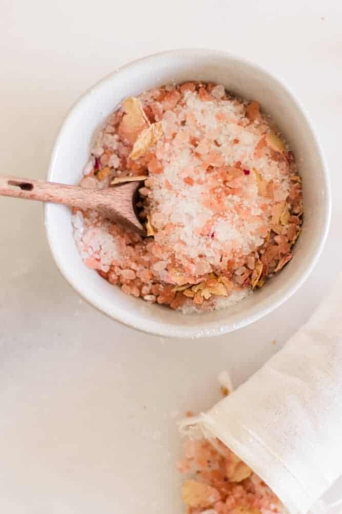 Small white bowl of rose bath salts with wooden spoon in it.