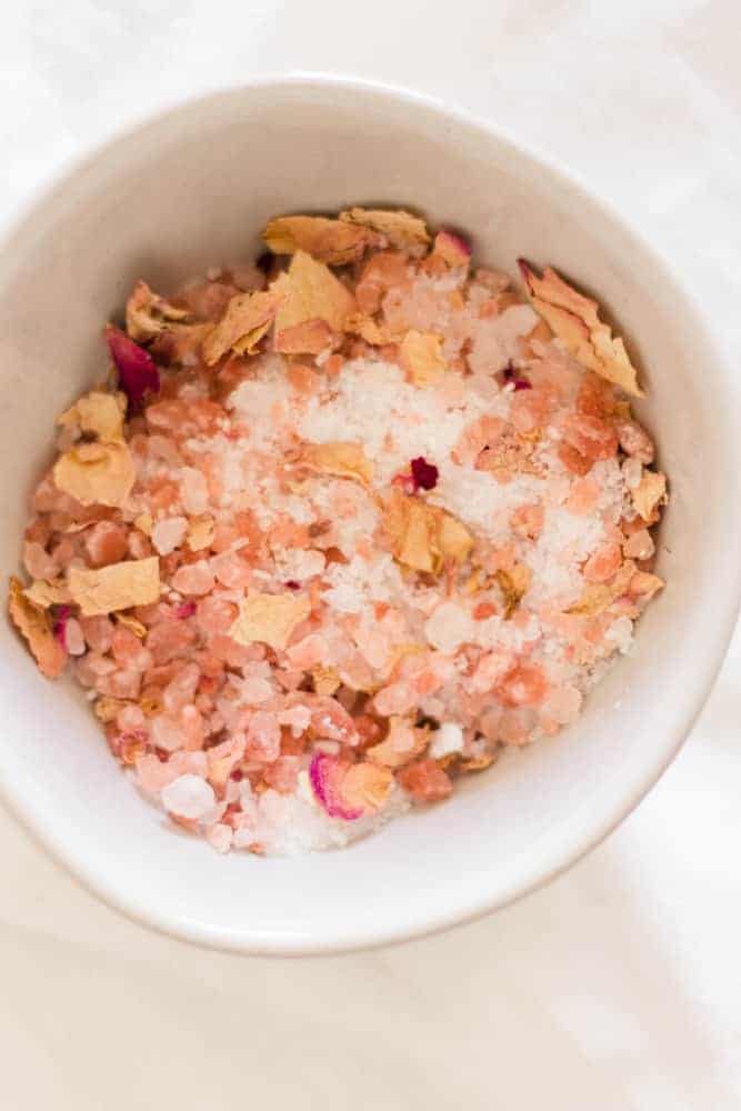 Pink salt and rose petal salt bath soak in small bowl .