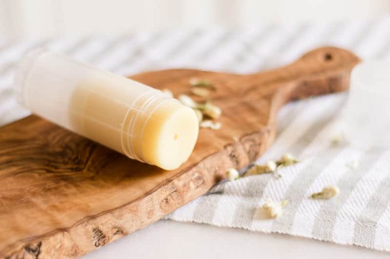 Foot balm stick laying on table with jasmine flowers around it. 