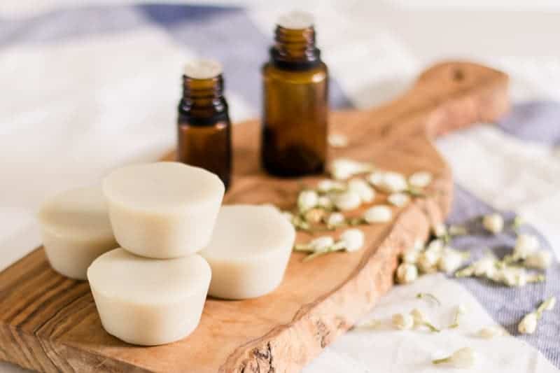 DIY lotion bars and essential oil bottles sitting on wood board with jasmine flowers around them. 