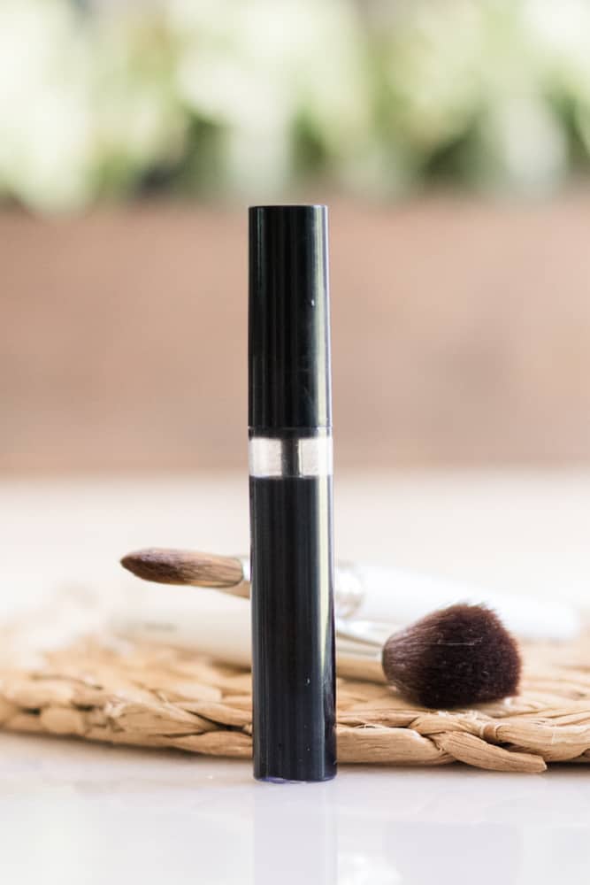 Homemade mascara in mascara bottle with makeup brushes behind it.