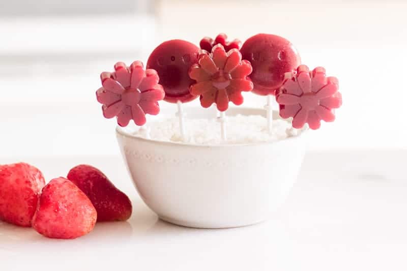 Homemade strawberry lollipops in standing in white bowl.