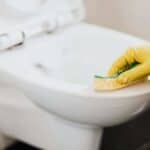 Scrubbing a toilet with foaming toilet cleaner and a sponge.