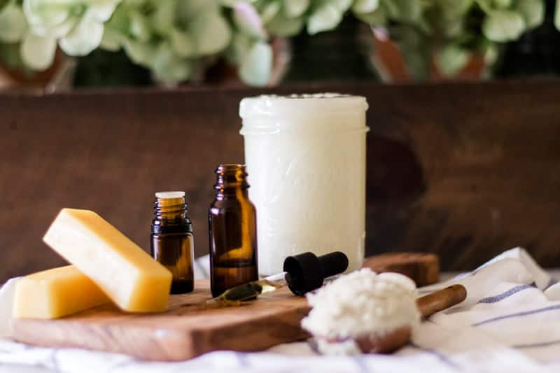 Jar of coconut oil, beeswax, vitamin E oil and essential oils sitting on table. 