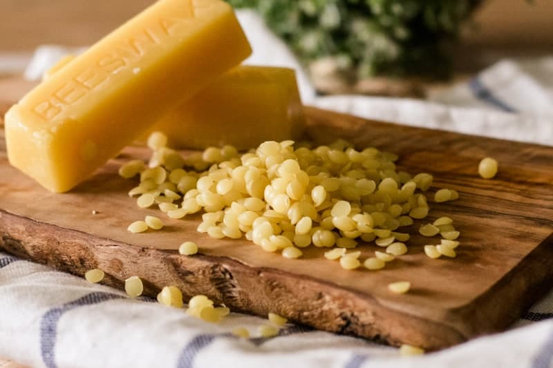 Beeswax pellets and beeswax bars on wooden board. 