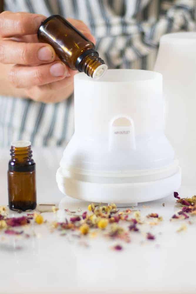 White diffuser on marble table with amber colored essential oil bottles next to it and flower buds sprinkled around it. 