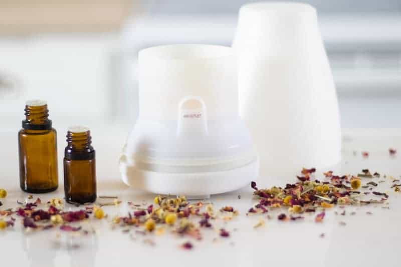 White essential oil diffuser on marble table with dried petals around it. 