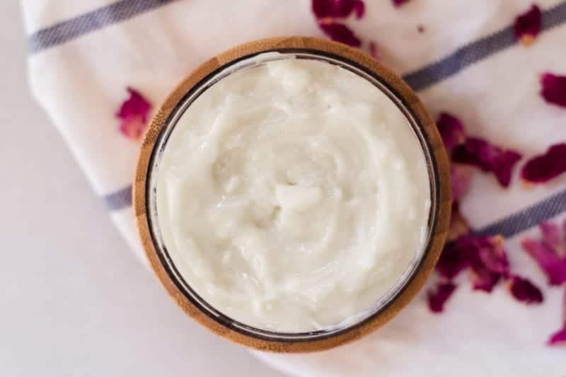 Homemade styling hair cream in small container with rose petals around it. 