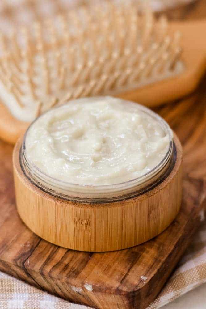 DIY hair styling cream in small wooden container with tan hair brush behind it. 