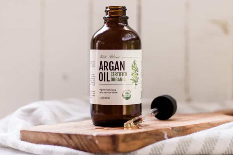 Bottle of argan oil sitting wood cutting board. 