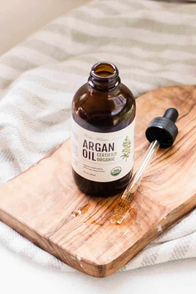 Amber glass bottle of argan oil on wooden cutting board. 