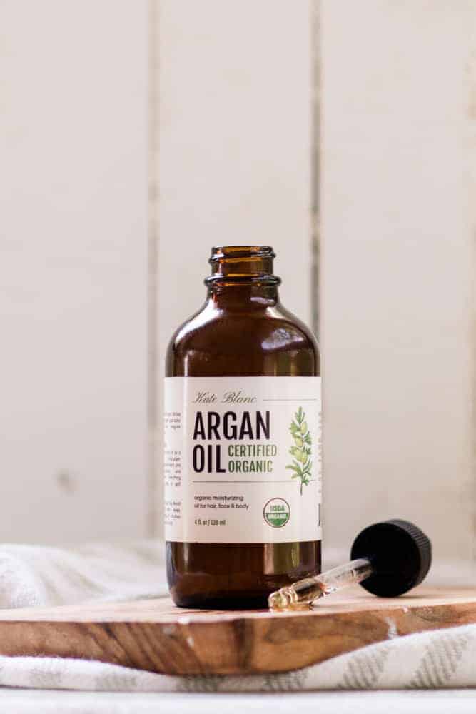 Argan bottle open with dropper of argan oil in front of it. 