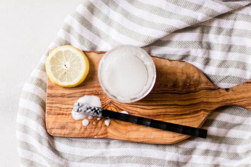 Baking soda and hydrogen peroxide mixed together and small mason jar sitting on wood board with a lemon slice and black toothbrush. 