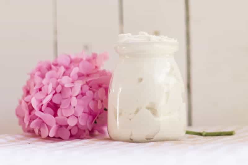 Small glass jar of tallow whipped body butter on table with pink flowers behind it.