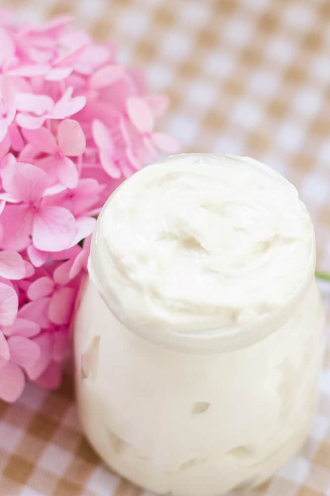 Creamy white tallow body butter in little glass jar with pink flowers behind it.